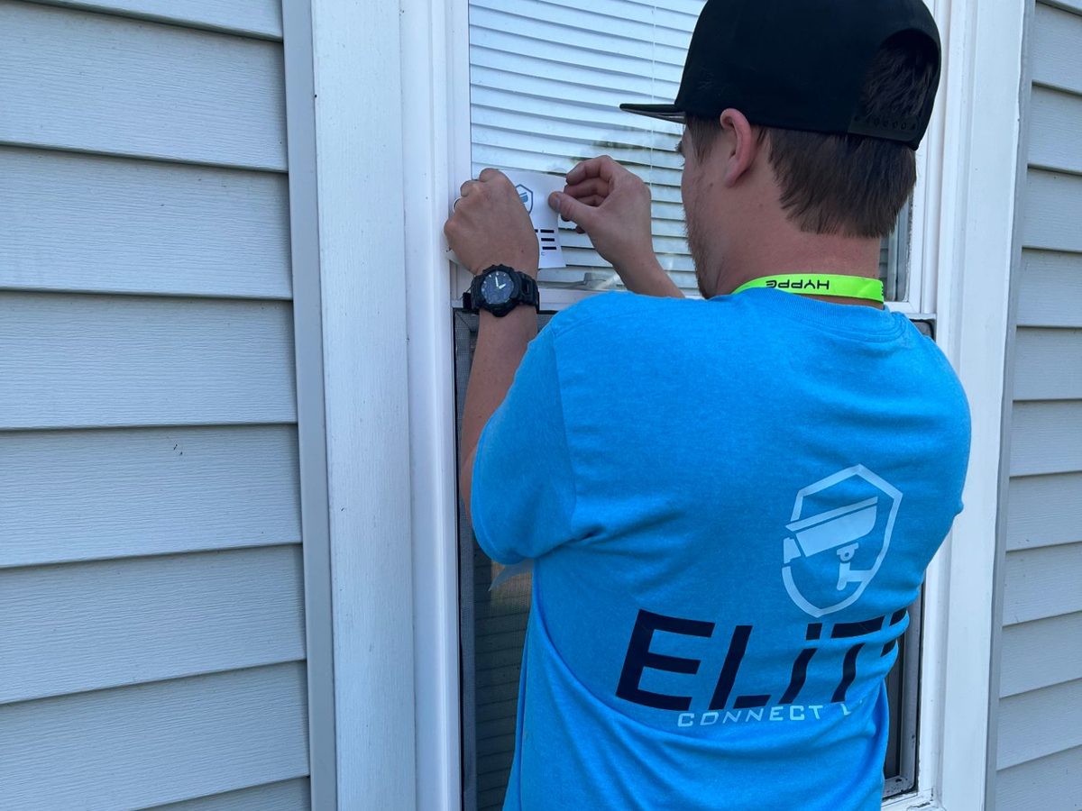Elite Connect technician in a company shirt applying a security decal to a home's window