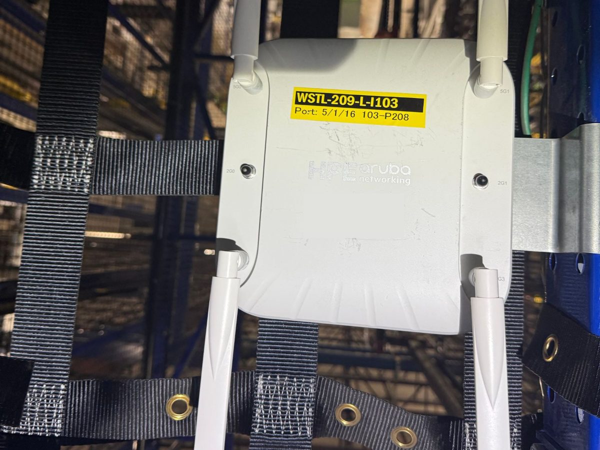 Aruba access point mounted on warehouse racking, labeled with its name and switch port